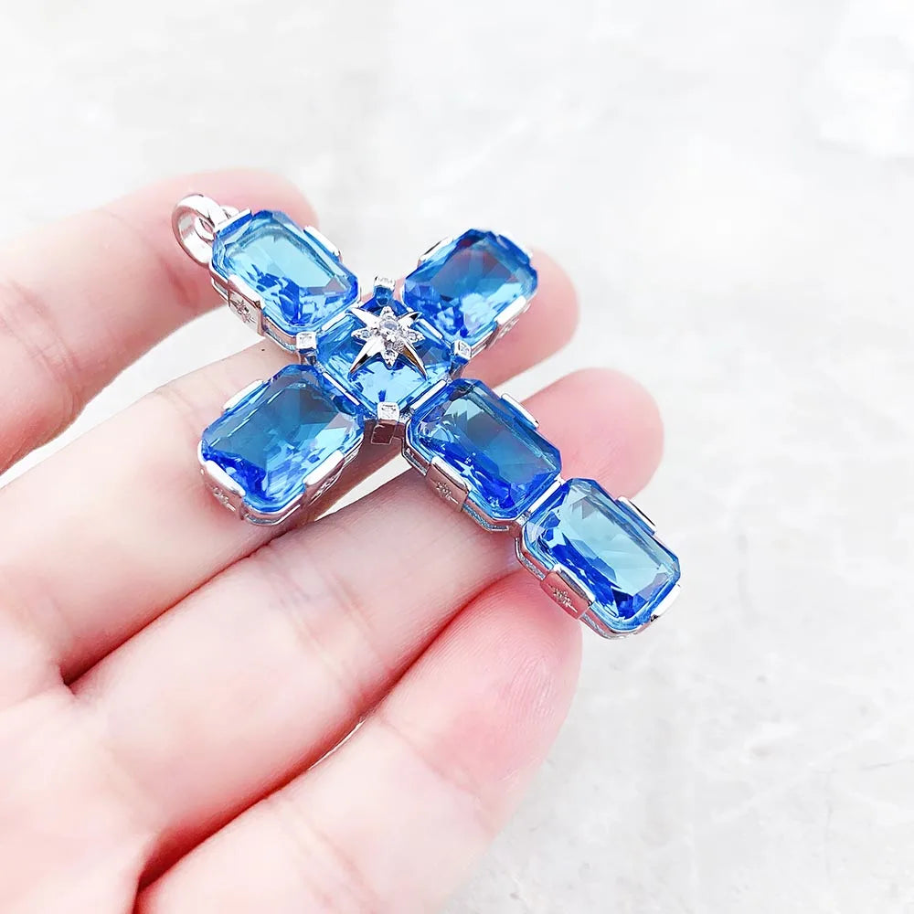 Kreuz-Anhänger in Hand gehalten: silbernes Kreuz mit blauen Steinen und Stern