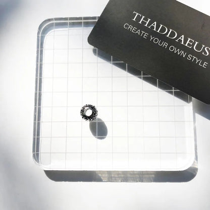 Silberner Charm an Schmuckkarte, rundes Ornament in dunklem Muster