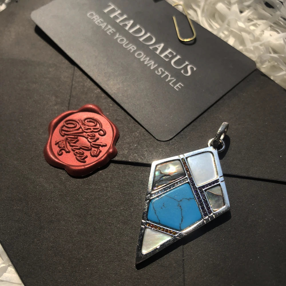 Silberner geometrischer Anhänger mit blauem Einsatz und rotem Schmuckdetail daneben
