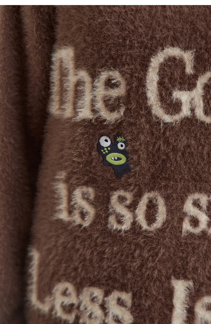 Camelfarbener Damenpullover im Detail mit Schriftzug und großem grünen Motiv-Emblem