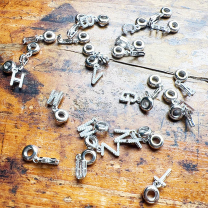 Mehrere silberne Buchstaben-Charm-Anhänger mit hellem Steinbesatz, an Kettenösen
