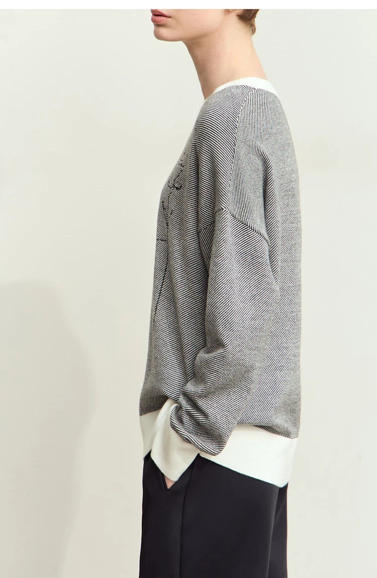 Seitenansicht: grauer Strickpullover mit weißem Kontrastbund und dezenter Stickerei