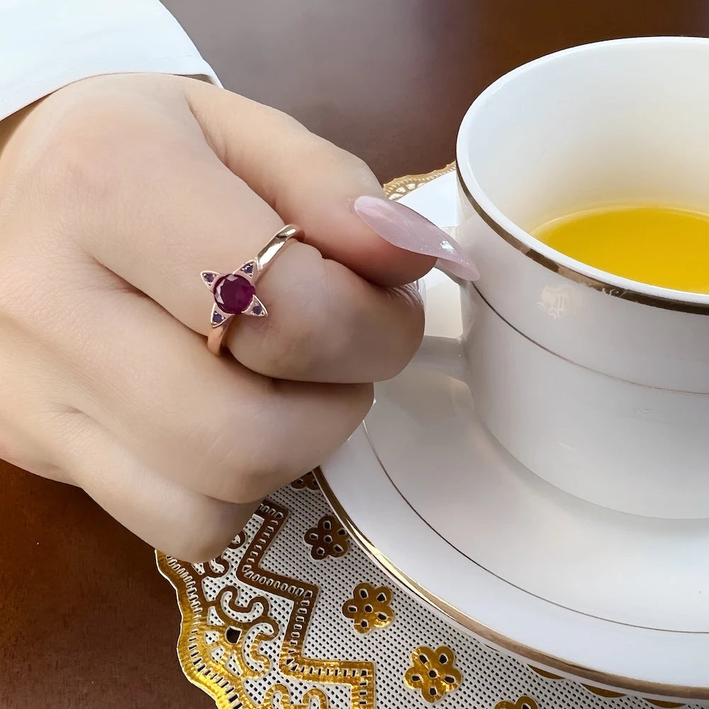 Roségoldfarbener Ring mit violettem Stein und umrandenden Ziersteinen am Finger