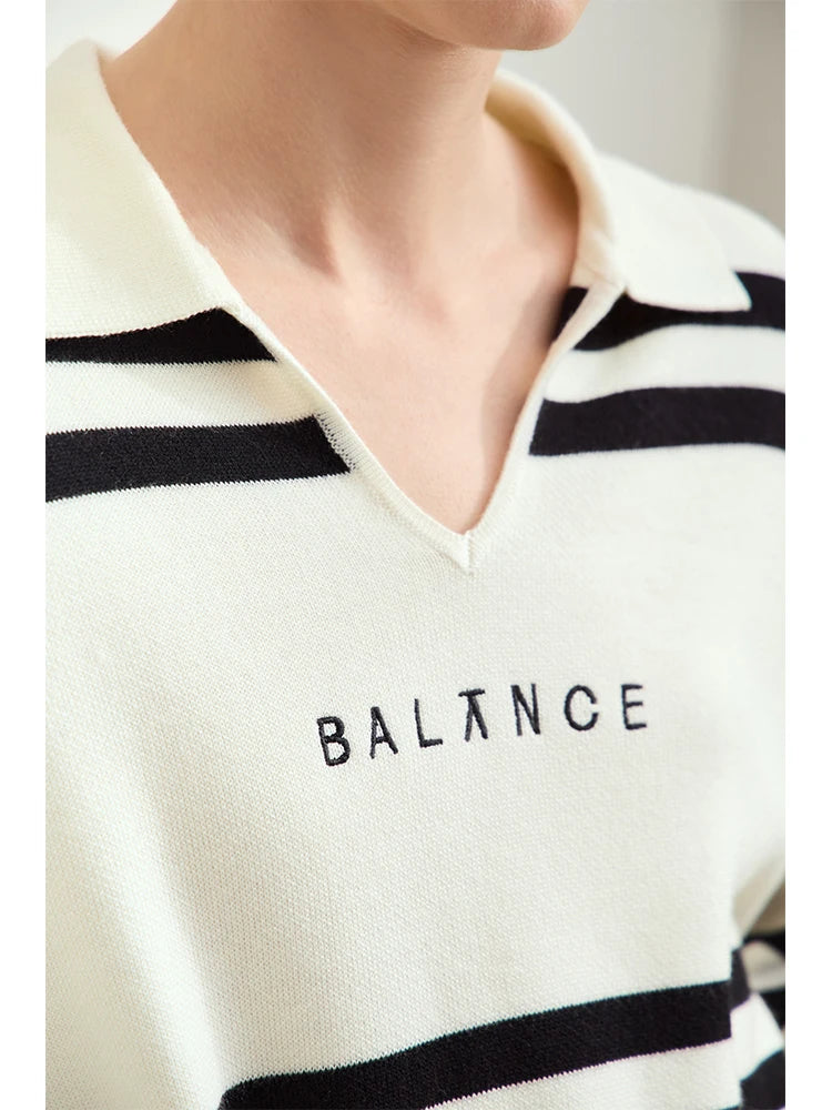 V-Ausschnitt-Pullover im Detail: Streifenmuster und Stickerei „BALNCE“ auf cremefarbenem Stoff.