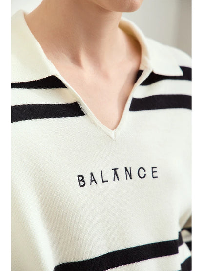 V-Ausschnitt-Pullover im Detail: Streifenmuster und Stickerei „BALNCE“ auf cremefarbenem Stoff.
