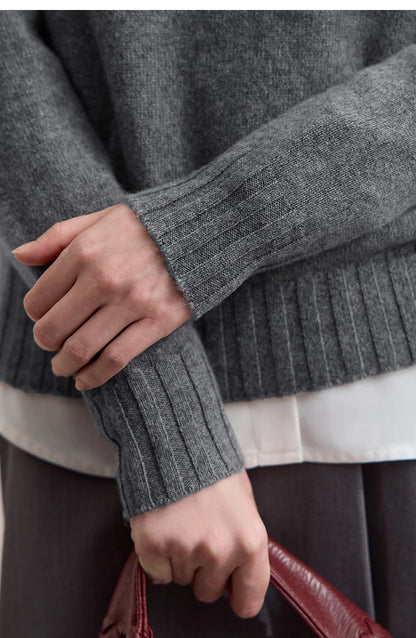 Nahaufnahme: Grauer Strickpullover mit geripptem Ärmelbündchen und weißem Unterteil am Saum.