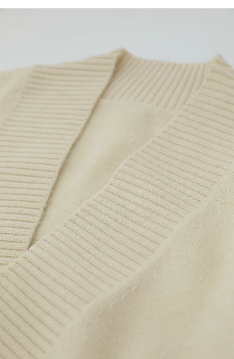Nahaufnahme V-Ausschnitt: cremefarbener Strickpullover mit eingewebtem Zopfmuster