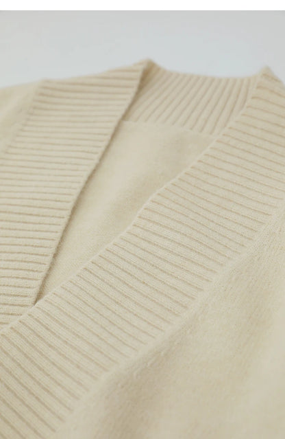 Nahaufnahme V-Ausschnitt: cremefarbener Strickpullover mit eingewebtem Zopfmuster