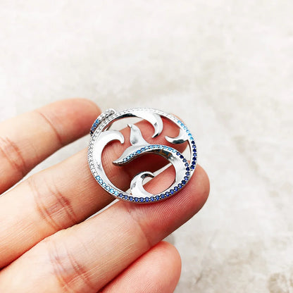 Delfin-Anhänger in der Hand, rundes Motiv aus Sterlingsilber mit blauen Steinen