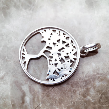 Silberfarbener Anhänger mit Baum-Silhouette im Kreis und seitlicher Öse