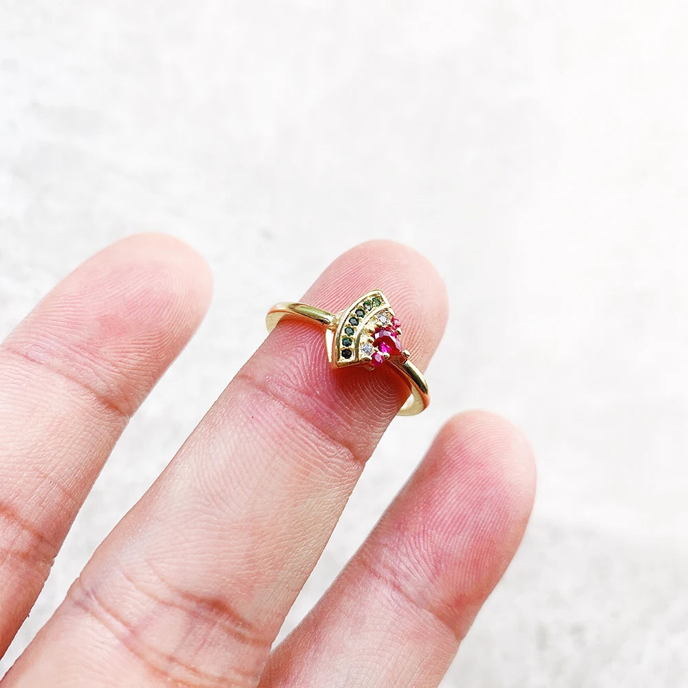 Goldfarbener Ring mit pinkem Stein und grüner Besatzung, Detailansicht am Finger