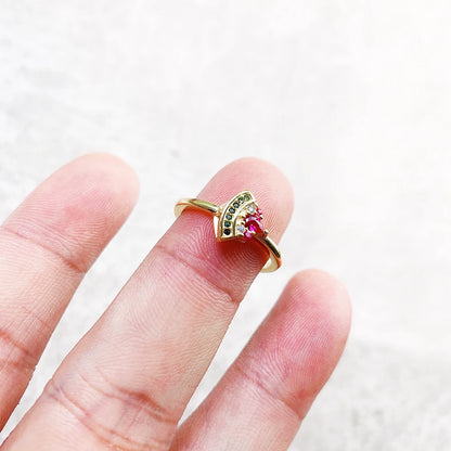Goldfarbener Ring mit pinkem Stein und grüner Besatzung, Detailansicht am Finger