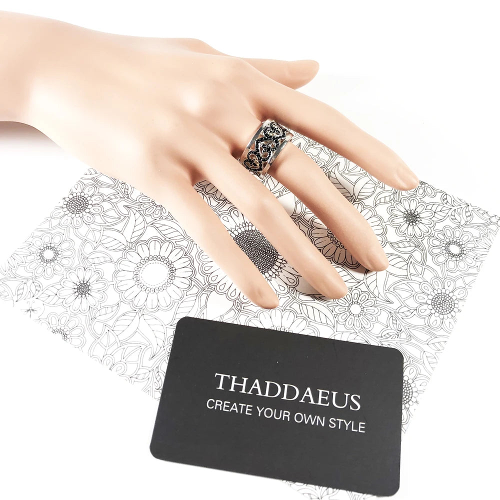 Silberner Ring am Finger mit schwarzem Arabesque-Herz-Motiv und dekoriertem Band