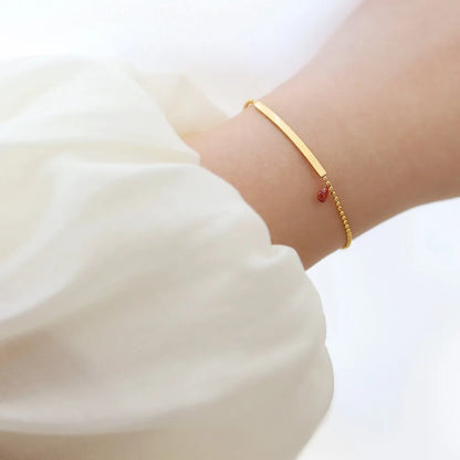 Goldfarbenes Armband am Handgelenk mit rotem Zirkonia-Herz und feiner Kette