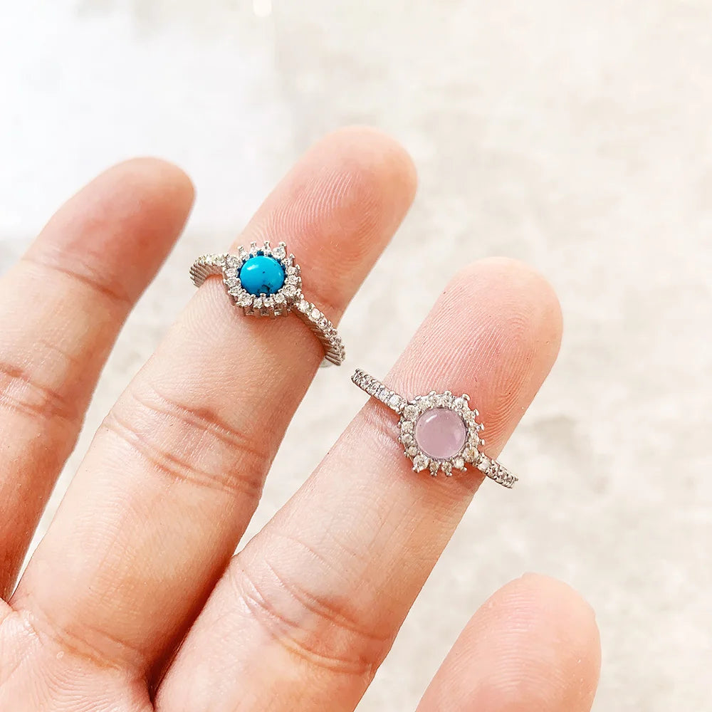 Silberne Ringe auf Fingern: blau runder Stein und rosafarbener Stein im Strahlenkranz