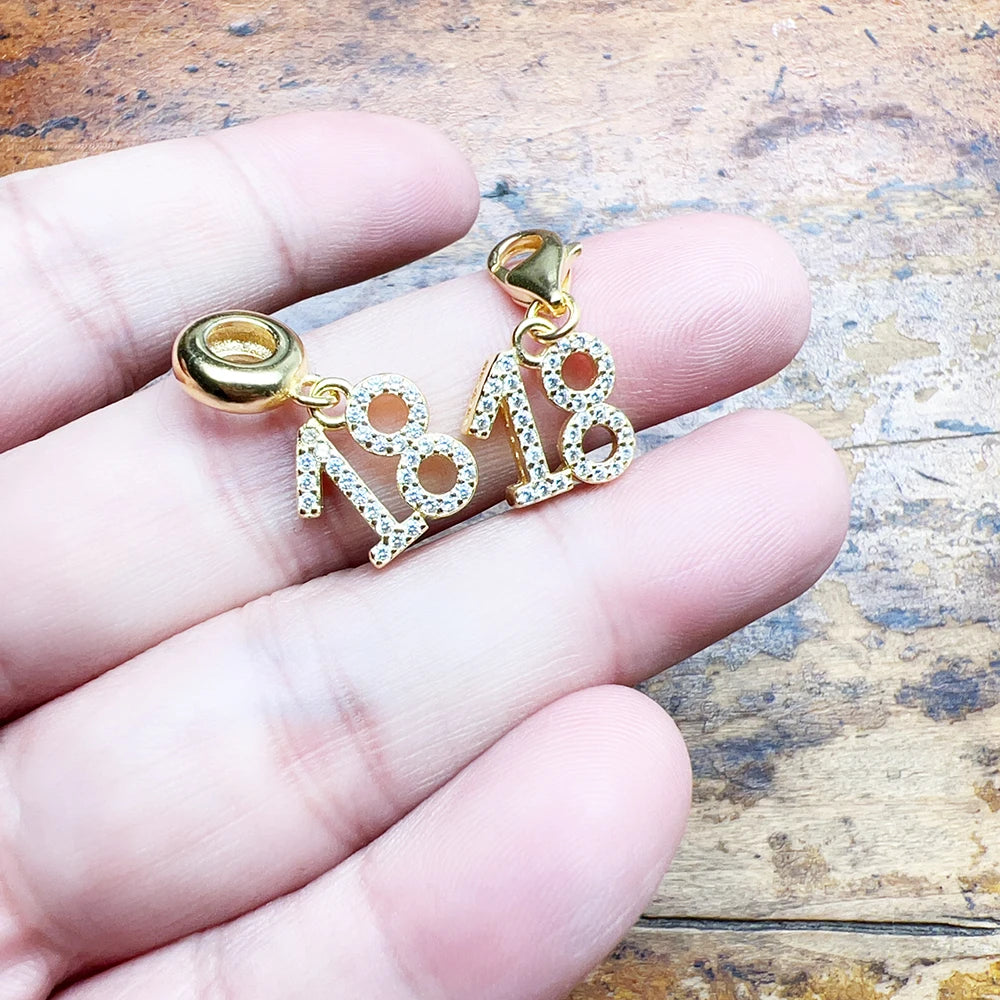 Charm-Anhänger Nummer 18, vergoldet, mit funkelnden Steinen, in der Hand gehalten
