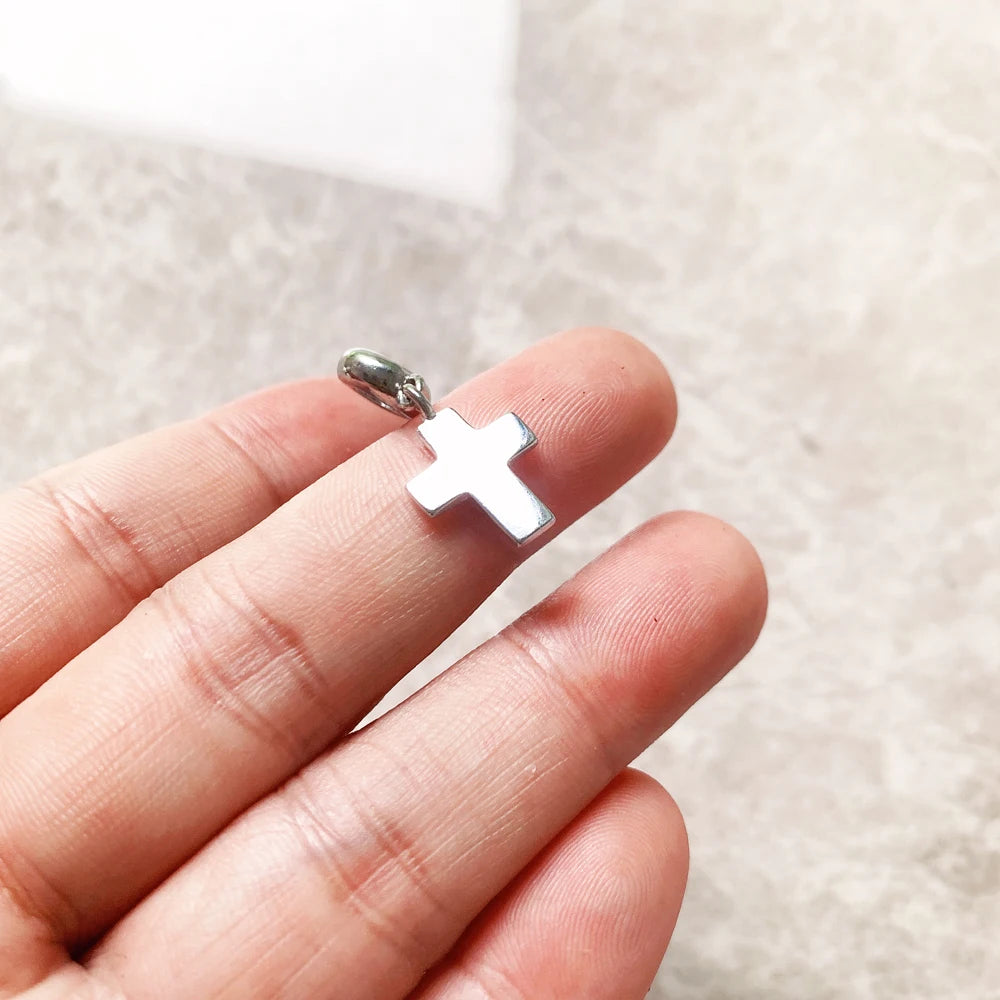 Kleiner Kreuz-Anhänger silber an der Hand, Öse sichtbar, kompakte Kreuzform