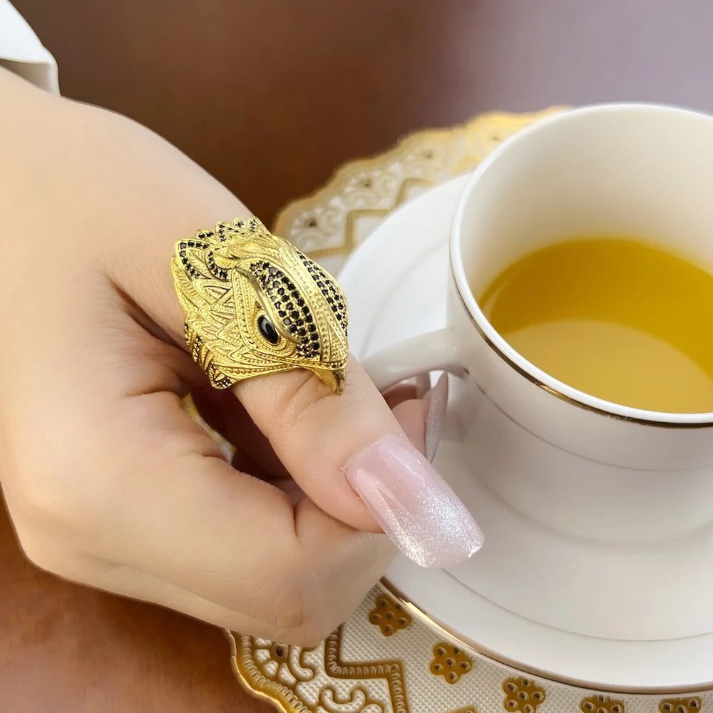 Goldfarbener Cocktailring mit Eulenkopf und schwarzem Auge, nah an Finger