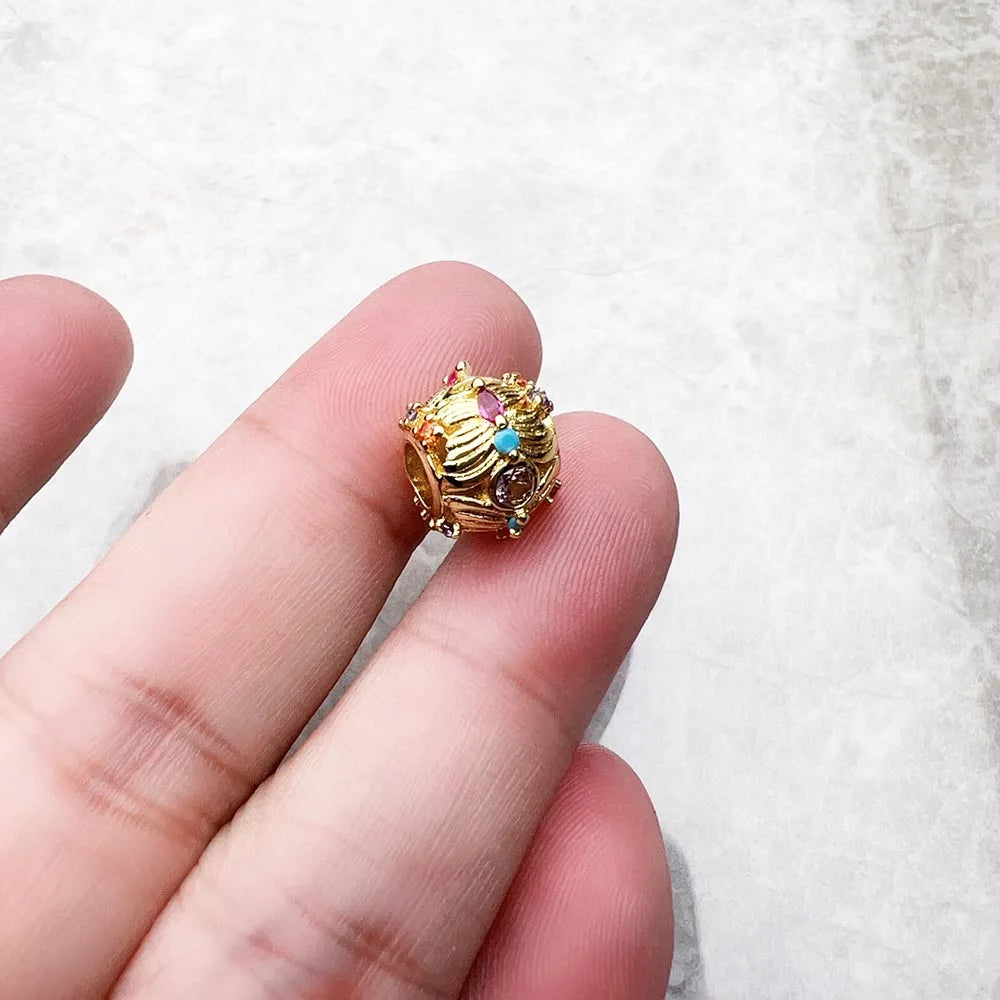 Goldfarbene Schmuckperle in der Hand, mit bunten Zirkonia-Steinen