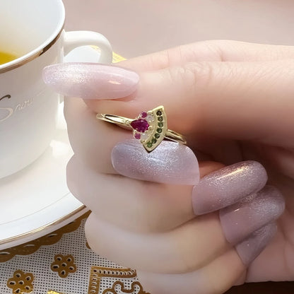 Goldfarbener Ring mit pinkem Stein und grünen Ziersteinen am Finger getragen