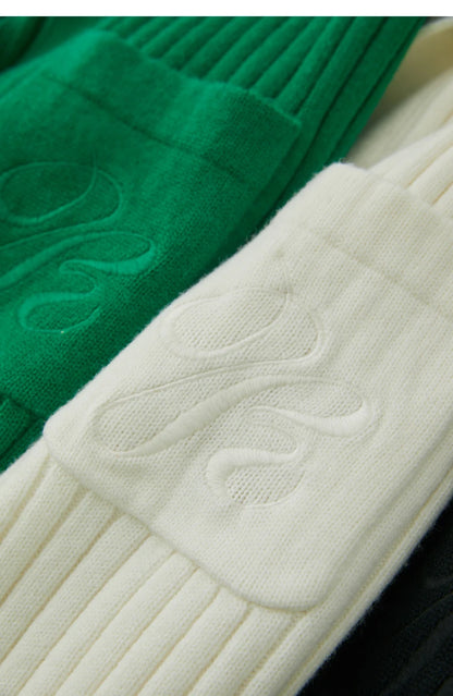 Detail: Weißer Strickärmel mit reliefartiger Stickerei und Rippenmuster am Pullover