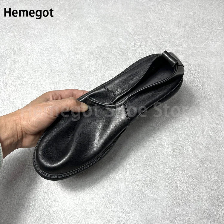Schwarzer Leder-Loafer seitlich, Hand hält den Schlupfbereich, flache Sohle