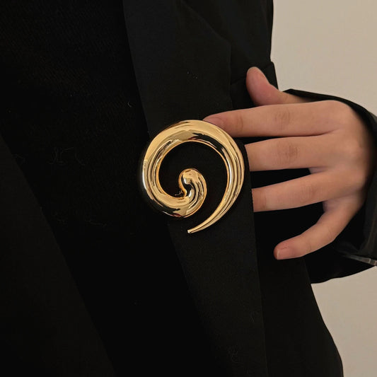 Vergoldete Spiral-Vortex-Brosche mit unregelmäßigem Wirbel-Design auf schwarzem Stoff