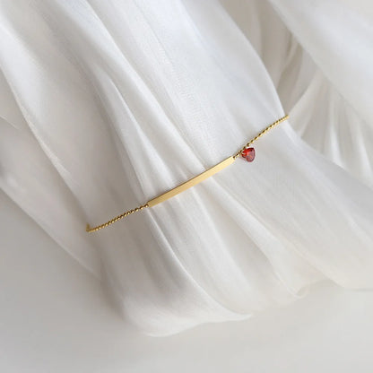 Damenarmband auf Stoff drapiert: goldfarbene Stange mit rotem Herz-Zirkonia