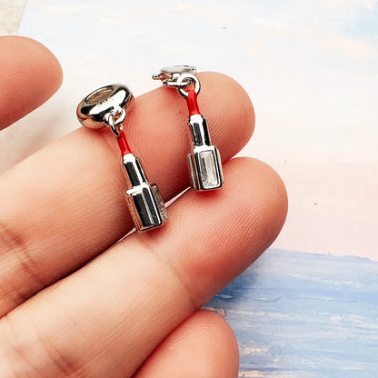 Nahaufnahme: Zwei silberne Charm-Anhänger mit rotem Lippenstift-Detail auf Hand