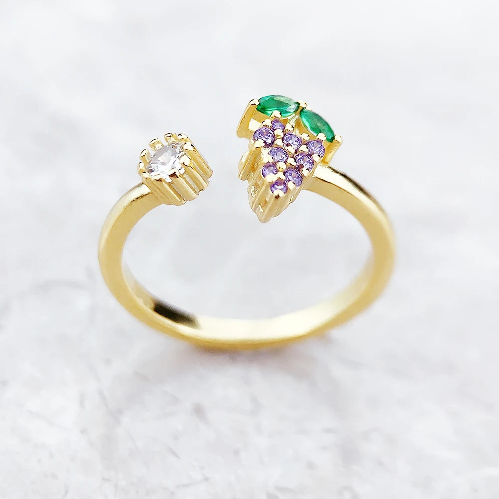 Nahaufnahme: goldfarbener Ring mit Grünstein und violetten Traubensteinen