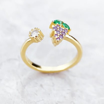 Nahaufnahme: goldfarbener Ring mit Grünstein und violetten Traubensteinen