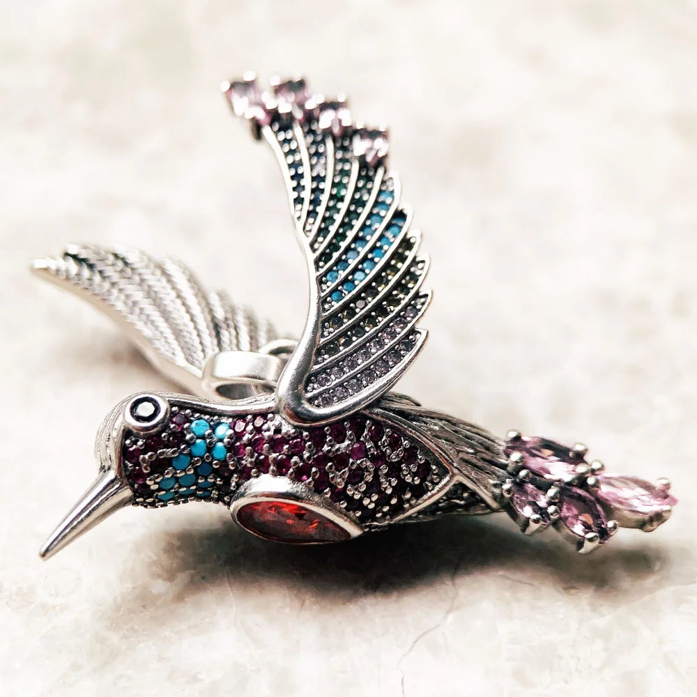 Kolibri-Anhänger im Detail, silbern mit türkisfarbenem Kopf und pinkem Flügelstein