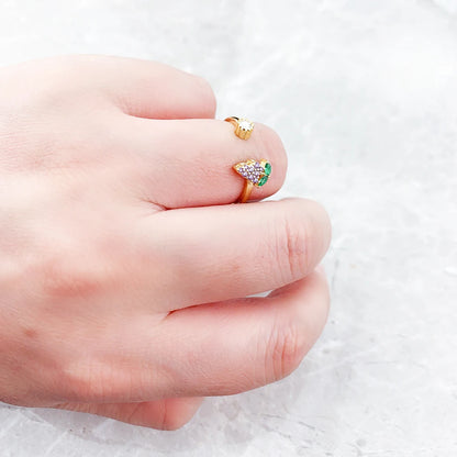 Ring in der Hand gehalten: goldfarbener Schmuck mit grünem Stein und violetten Details