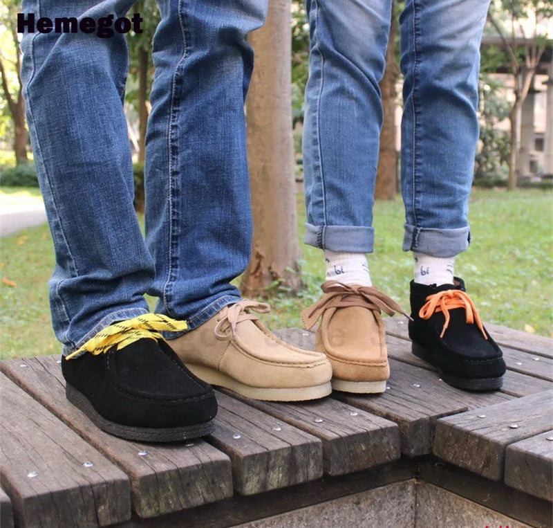 Herren-Schnür-Kurzstiefeletten: beige Paar und schwarze Alternative, getragen auf Holzpflaster