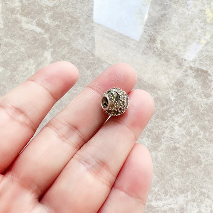 Gelb-grüner Strass-Charme auf silberfarbenem Metall, auf der Hand gehalten