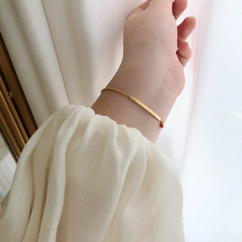 Goldfarbenes Damenarmband am Handgelenk mit rotem Zirkonia und schmaler Stange