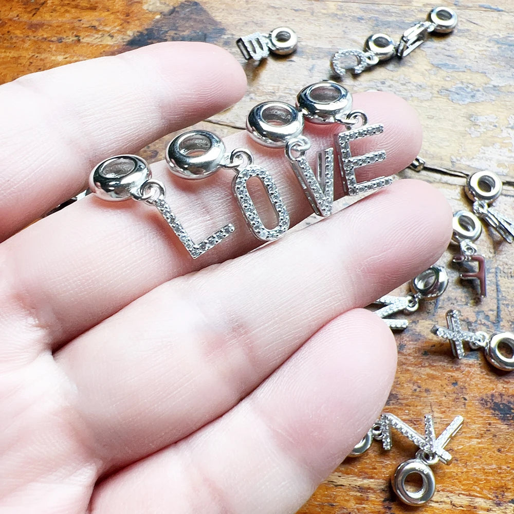 Silberner Buchstaben-Charm-Anhänger mit hellem Steinbesatz, in einer Hand gehalten