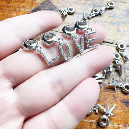 Silberner Buchstaben-Charm-Anhänger mit hellem Steinbesatz, in einer Hand gehalten
