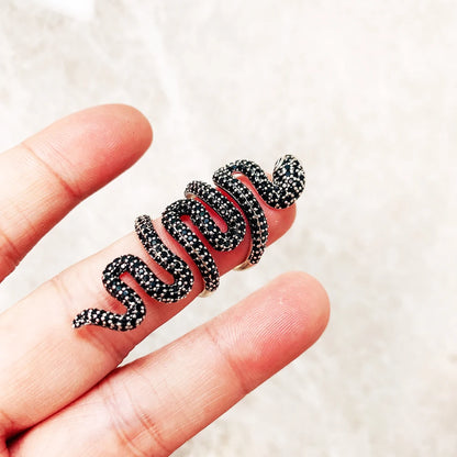 Schwarzer Schlangenring mit roten Akzenten und Steinbesatz, in Händen gehalten