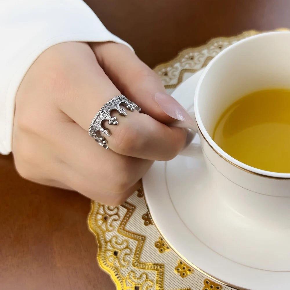 Kronenring aus 925-Silber am Finger, Hand in Nähe einer Teetasse