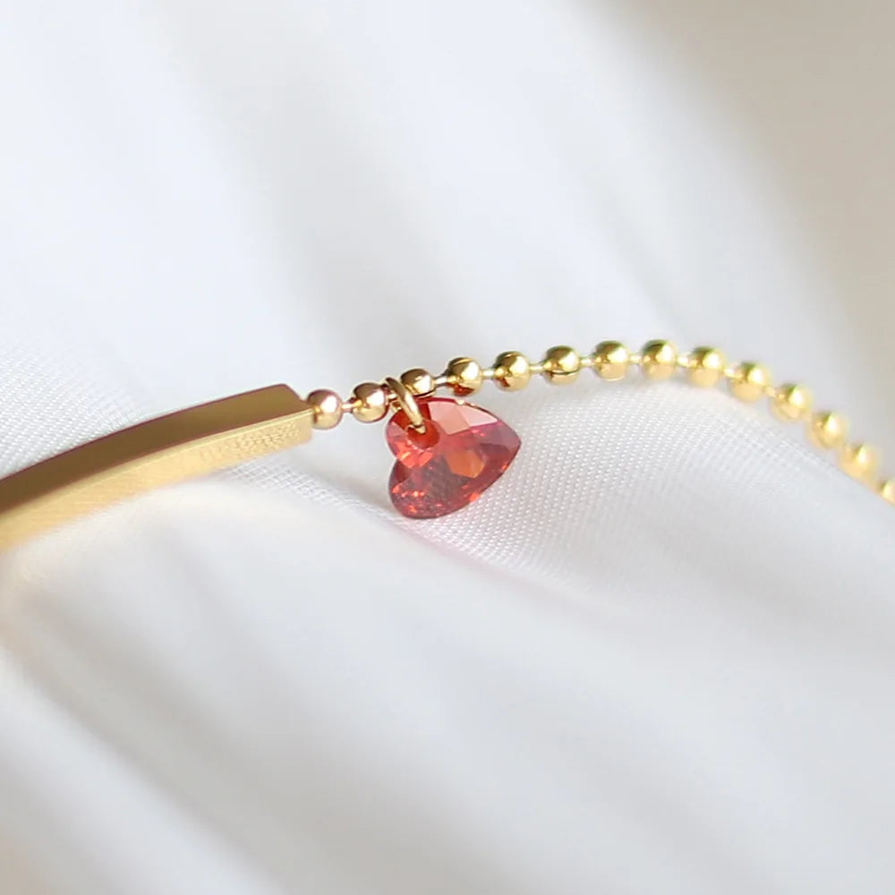 Goldfarbenes Armband im Detail: rotes Zirkonia-Herz und Kugelkette