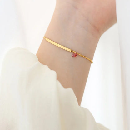 Damenarmband am Handgelenk: schmale goldfarbene Stange mit rotem Herzstein
