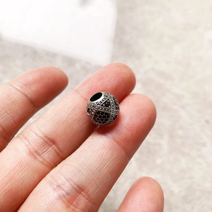 Silberne Charms-Perle mit schwarzem Zentrum und geometrischem Muster, auf Finger