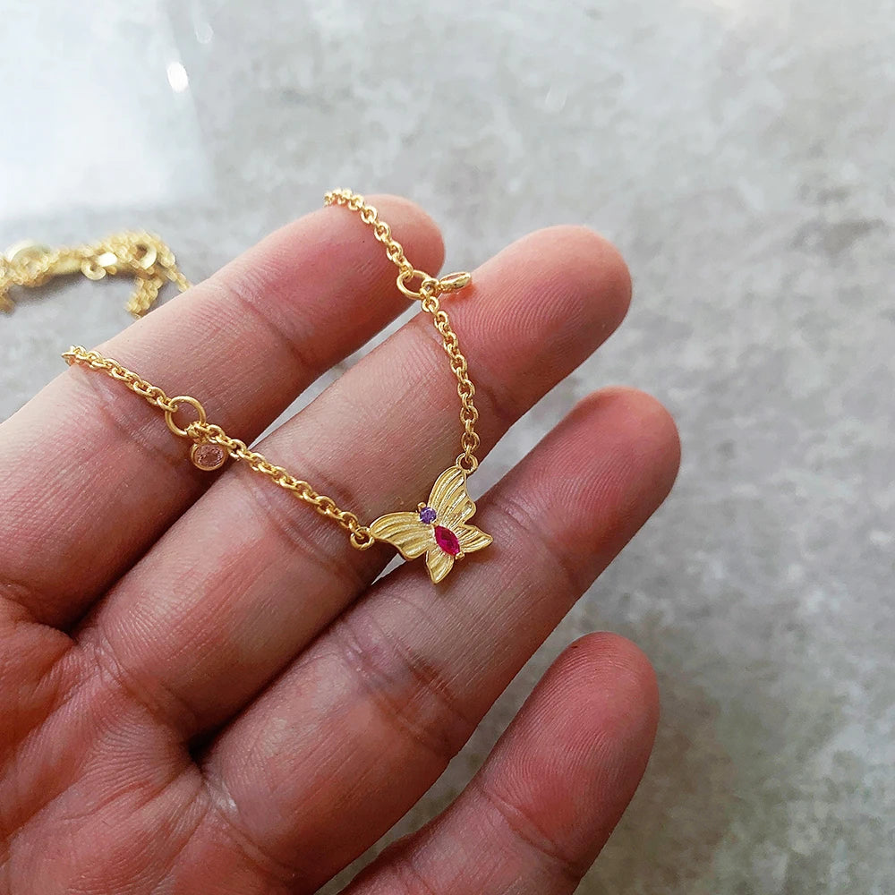 Goldfarbene Halskette mit Schmetterlings-Anhänger und rosa-lila Steinen in Hand