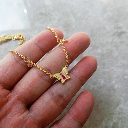 Goldfarbene Halskette mit Schmetterlings-Anhänger und rosa-lila Steinen in Hand