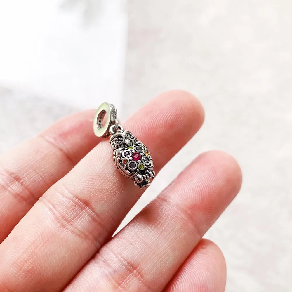 Silberner Eulen-Charm in der Hand, mit bunten Steinen und breiter Öse