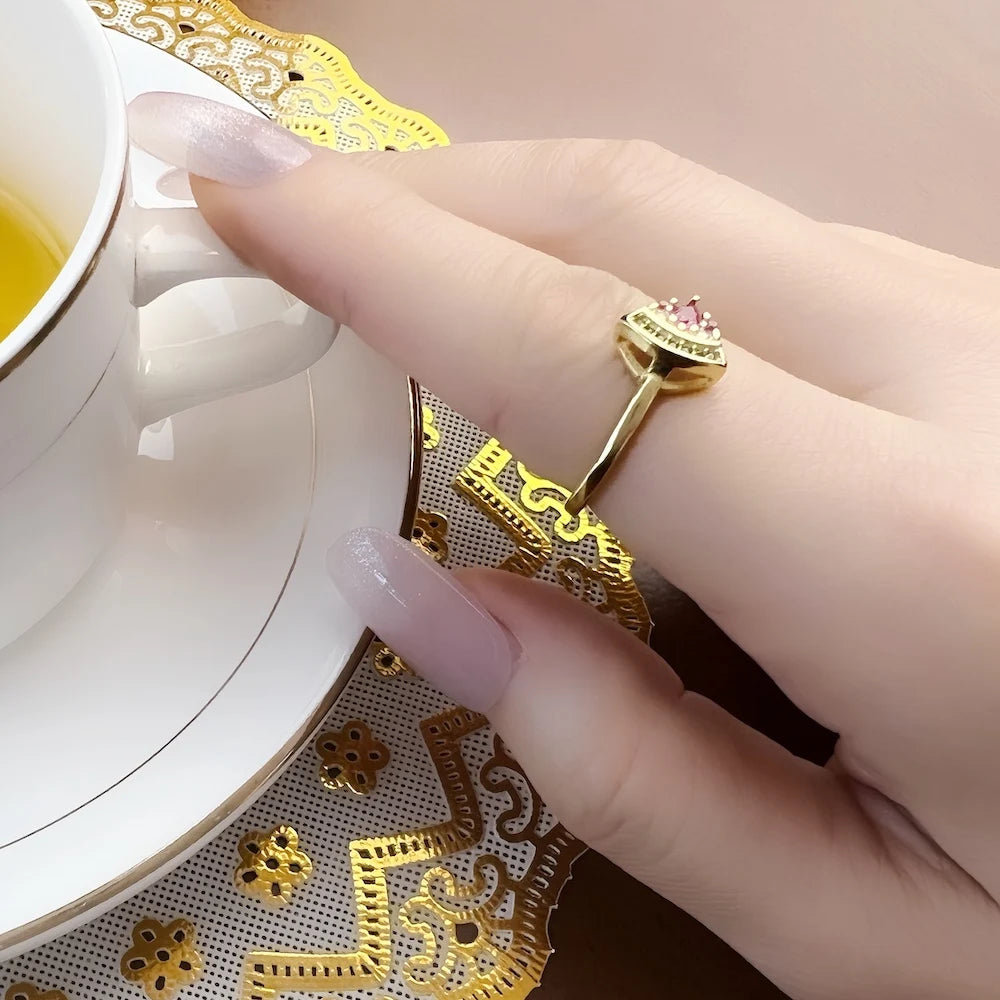 Goldfarbener Ring mit pinkem Stein und grüner Verzierung, seitlich am Finger
