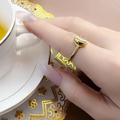 Goldfarbener Ring mit pinkem Stein und grüner Verzierung, seitlich am Finger