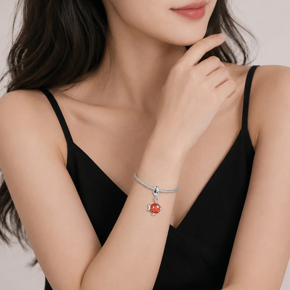 Silbernes Armband mit rotem Fischanhänger am Handgelenk, feine Kette
